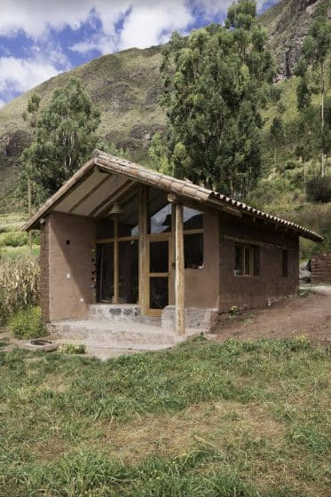 Pequeña cabaña rústica ubicada en la montaña, construida con adobe y techo de tejas de barro.